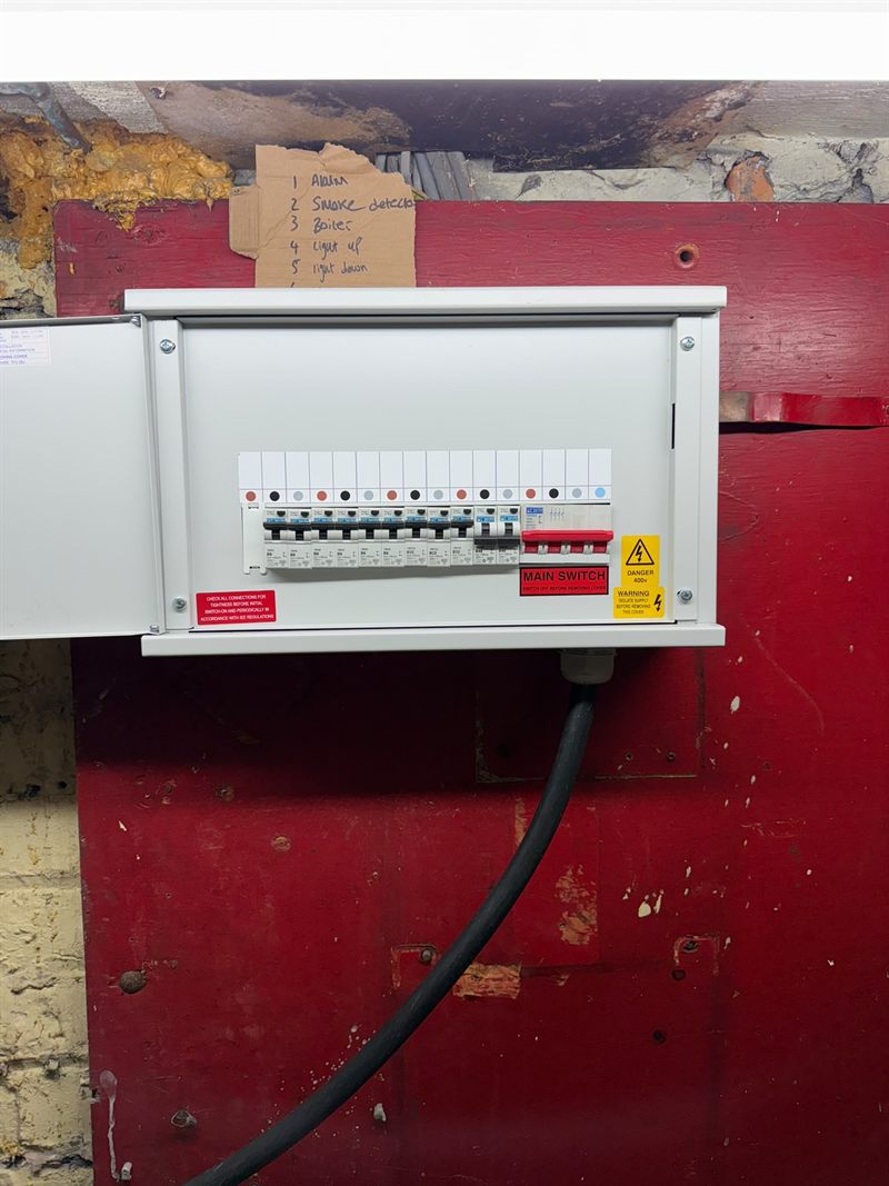 The finished three-phase board with the cover fitted, showing a full row of breakers, the main switch and the 400 volt warning label.